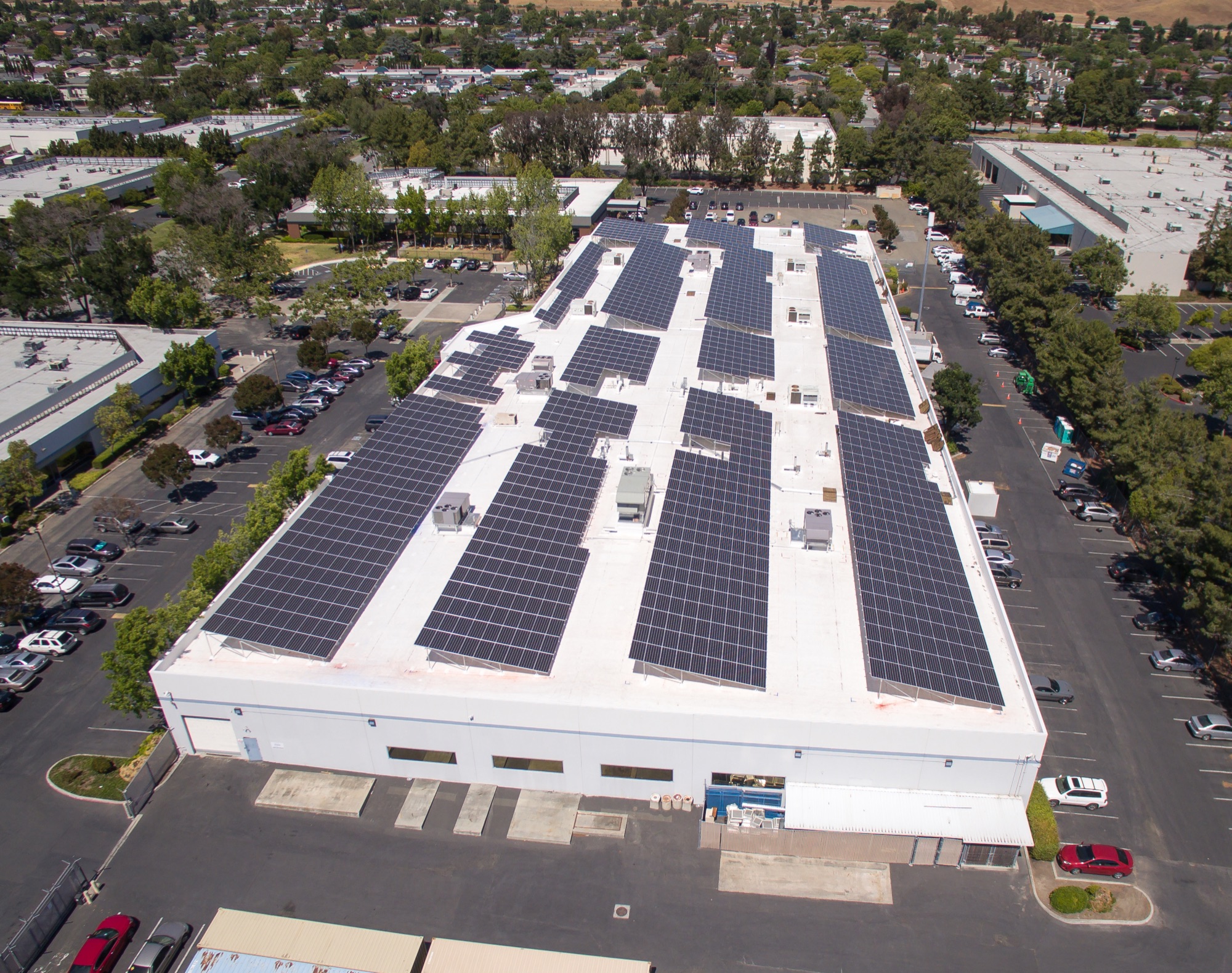 47951 Westinghouse Drive from the air. A white roof covered in solar, trees and parking around it.